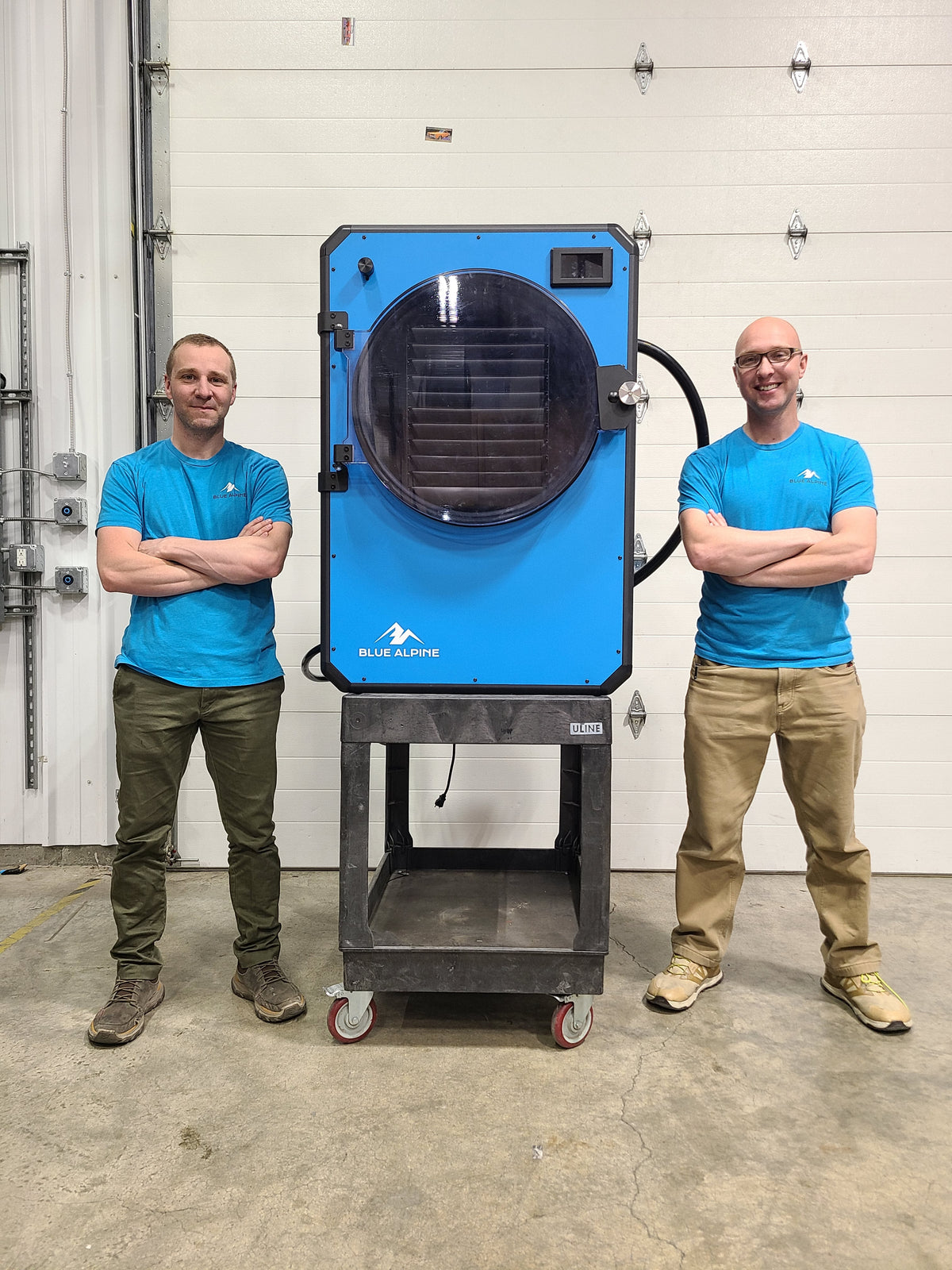Two men standing beside the Blue Alpine XL commercial freeze dryer on a stand